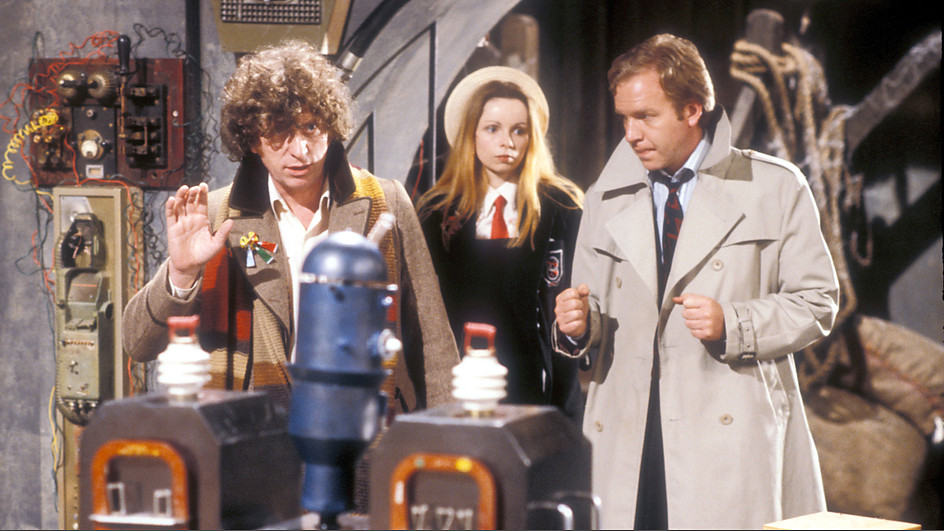 Screencap from City of Death: In a wooden basement, the Doctor, Romana, and Duggan (a man in a tan trenchcoat), examine some scientific apparatus.