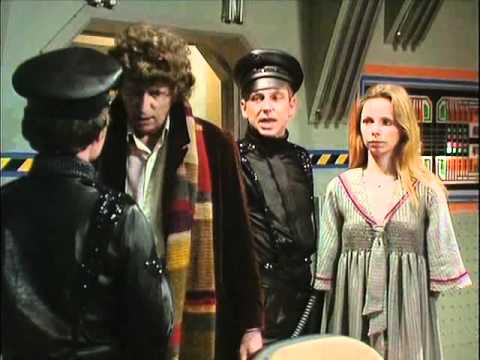 Screencap from Nightmare of Eden: In some sort of sci-fi cockpit, the Doctor and Romana are held up by police guards in black shiny outfits and caps.