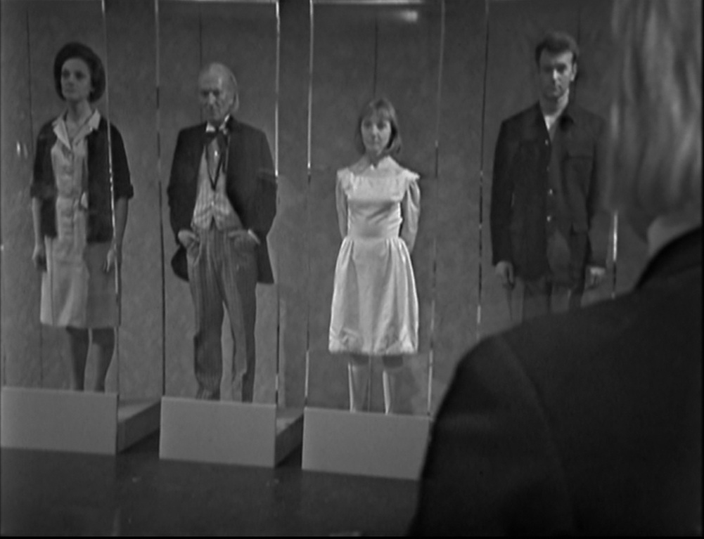 Screencap from The Space Museum: Barbara, the First Doctor, Vicki, and Ian stand in tall separate glass cases, uniform and staring into space.