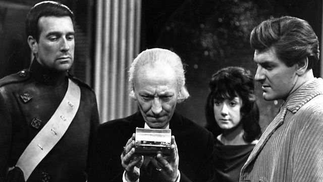 Screencap from Nightmare on Planet Kembel (episode 2: Day of Armageddon), showing our four heroes: from left to right, Bret Vyon (played by Nicholas Courtney in a sci-fi uniform); the Doctor, holding a small metal device; Katarina; and Steven. All four look at the device in the Doctor's hands.