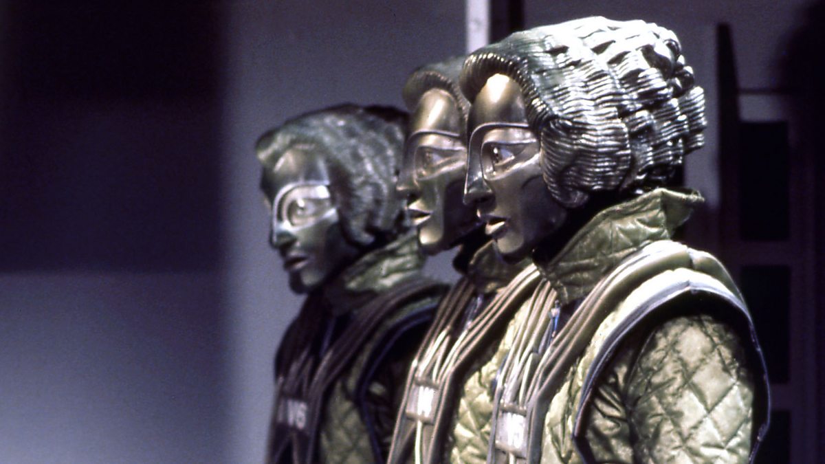 Screencap from The Robots of Death: Four silver humanoid robots with large eyes line up parallel to the camera.