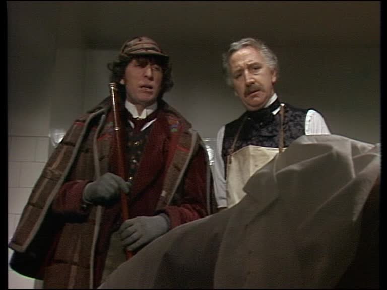 Screencap from The Talons of Weng-Chiang: The Doctor and Professor Litefoot, a gray-mustached Victorian gentleman, look down at a covered body.