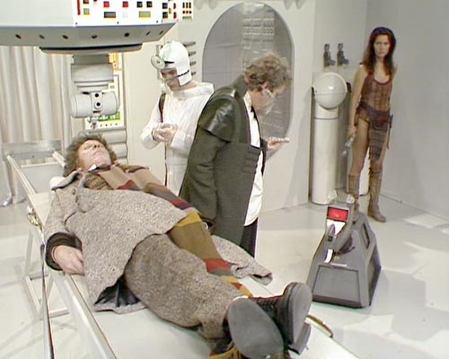Screencap from The Invisible Enemy: in a white hospital, the Doctor lies unconscious on a bed with a large machine suspended over his head. A man in a white outfit watches; another man in atweed coat with a goatee talks to K9, a metal dog. In the corner, Leela keeps watch.