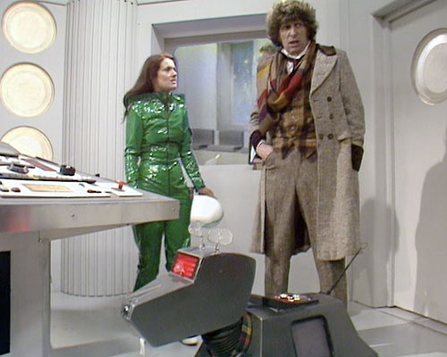 Screencap from The Invisible Enemy: in the TARDIS, the Doctor, K9, and Leela (wearing a shiny green outfit and holding a white cap) converse. Leela looks indignant or angry.