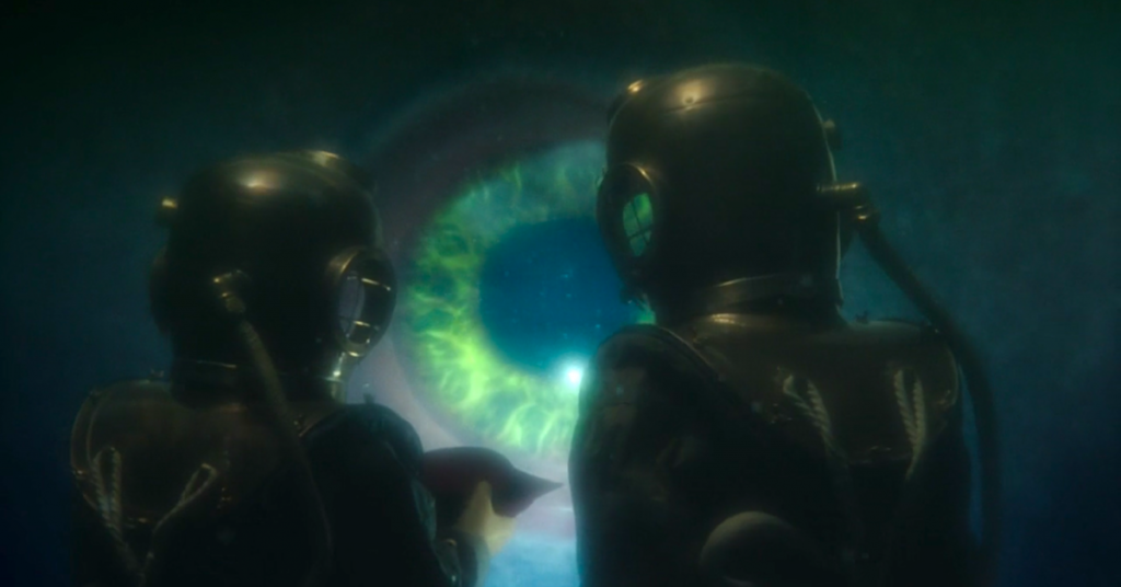 Screencap from Thin Ice: the Doctor and Bill, underwater in Victorian brass diving suits, stare away from the camera at a huge eye.